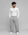 Man wearing a white long-sleeve shirt and gray sweatpants on a gray background