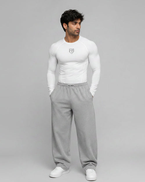 Man wearing a white long-sleeve shirt and gray sweatpants on a gray background